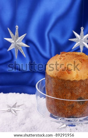 Christmas composition over a bright blue background: Panettone; a typical italian Christmas cake; served on a glass cake stand. Selective focus, shallow DOF