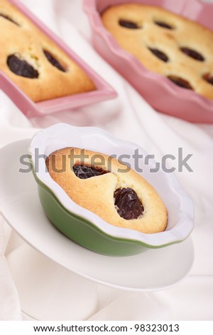 Small plum cake on a white cake stand. Plum cakes in pink pottery cake tins out of focus in the background. Selective focus, shallow DOF