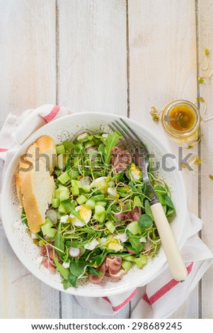 Rocket salad with ham and eggs, served in the white bowl ont the white wooden table.
