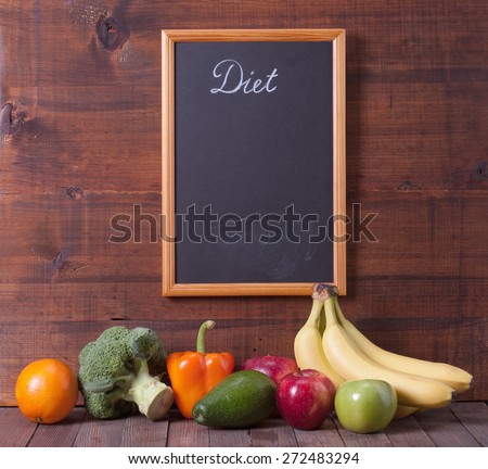 Black chalkboard for menu and fresh vegetables over wooden background. Diet food concept.