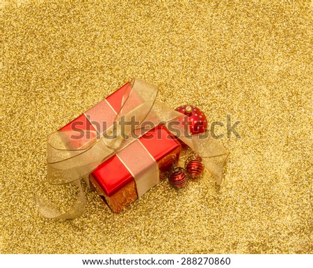 Red gift box and baubles with gold ribbon on a gold glitter background with copy space