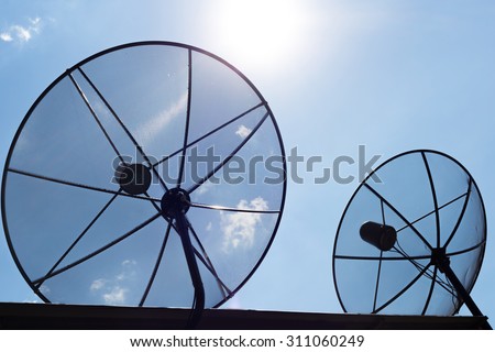 Two Satellite dishes communication technology network with sun and sky in background