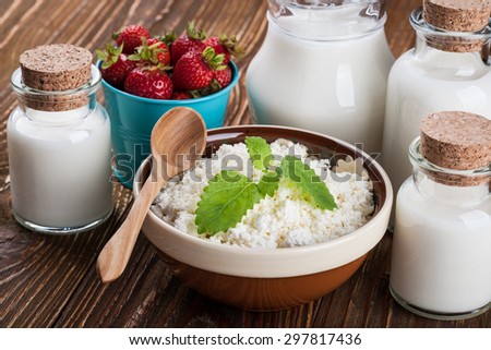 Bowl of cottage cheese, milk in glass container and a bucket of strawberries on wooden table