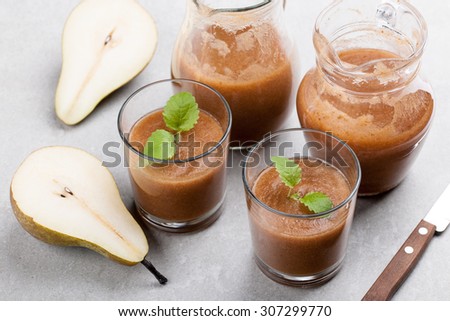 Two glasses of pear juices, glass pitcher and ripe pear on the ceramic surface