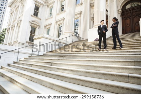 A well dressed man and woman converse on the steps of a legal or municipal building. Could be business or legal professionals or lawyer and client.