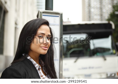 An attractive woman at a bus stop smiles at viewer.