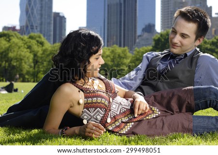 A young couple in the park lying on sides smile at each other. Focus on woman.