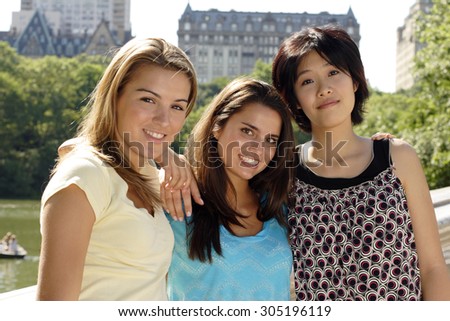 Three young women shoulder to shoulder on a park bridge.