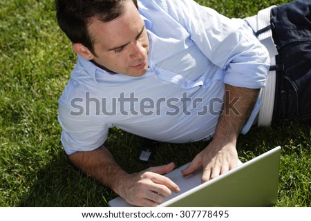 Man lies on grass with laptop.