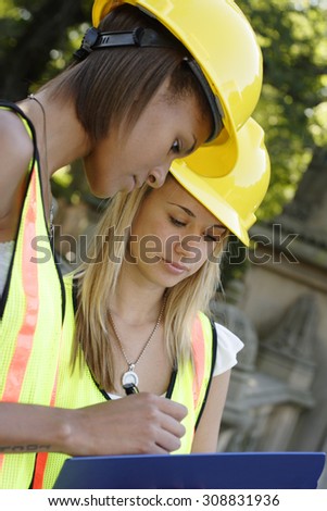 Two utility workers with clipboard smiling. Focus is on blond woman.