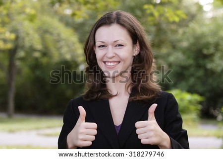 Young woman smiles and gives double thumbs up. Focus is on her face.