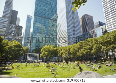 New York, New York, USA - June 30, 2011: People enjoying the weather on the Bryant Park lawn, surrounded by the tall buildings of Manhattan. Bryant Park sits behind the New York Public Library.