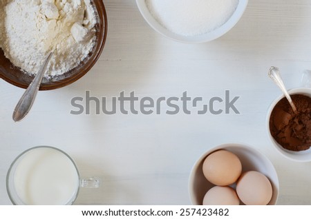Baking ingredients on a table: eggs, flour, milk, sugar, cacao.
