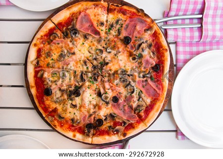 Delicious hot pizza with ham and mushrooms on wooden plate, on white table
