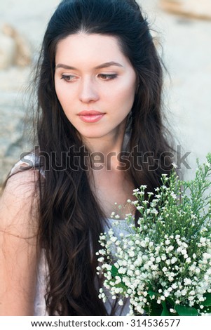 Romantic brunette woman in sunset wear white dress, holding bouquet of wildflowers