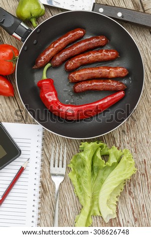 healthy Eating. frying pan with roasted Bavarian sausages and chili HOT PEPPER on  wooden background with vegetables and Tablet PC, notebook and pencil. business lunch