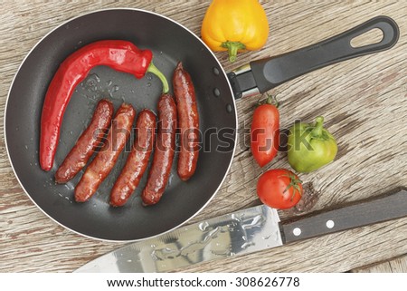 healthy Eating. frying pan with roasted Bavarian sausages and chili hot pepper on wooden background with vegetables.  business lunch