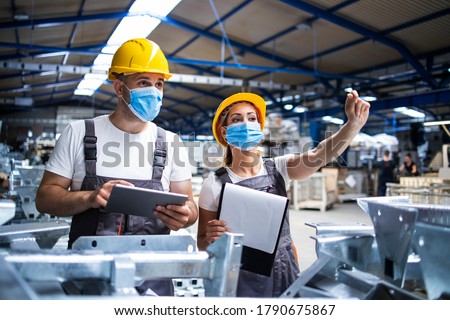 Factory workers with face masks protected against corona virus doing quality control of production in factory. People working during COVID-19 pandemic.