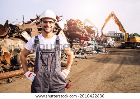 Portrait of worker standing in metal junk yard with crane lifting scrap metal for recycling. Foto d'archivio © 