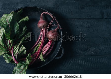 Beets with green tops in a black iron pan on a black wooden background