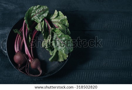 Beets with green tops in a black iron pan on a black wooden background