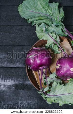 Kohlrabi cabbage with green tops on a metal plate on a black wooden background
