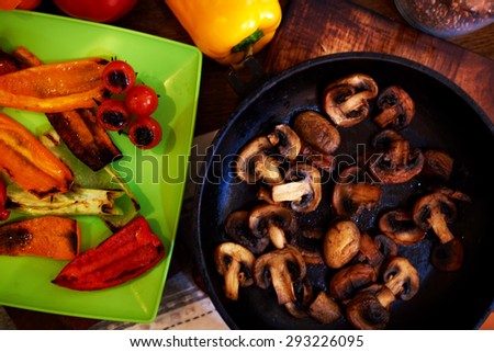 Mushrooms fried in a cast iron frying pan, pepper laid out side by side on the color green plate