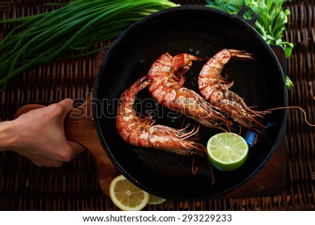 A young girl carries snacks on the table, it\'s Tiger prawns fried quickly over high heat in a cast iron frying pan and poured on top of a lemon