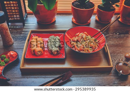 On the table is a wooden dressing on it two red plates with Japanese noodles with shrimp and sushi. Lunch in the office Sushi and Japanese rice noodles to order