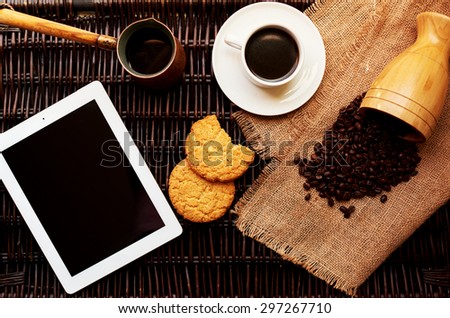 On a dark wicker rattan table, a light breakfast is served the plate, a cup of fresh coffee and a round oatmeal cookies