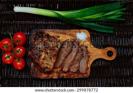 On the table lies a rattan board which served pork tenderloin baked in the oven in one piece, next leeks and cherry tomatoes from which cook fresh light salad