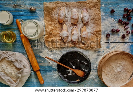 The situation in confectionery, will cook bagels stuffed with cherries, put them on paper for baking, lies next to the flour, milk is in the decanter