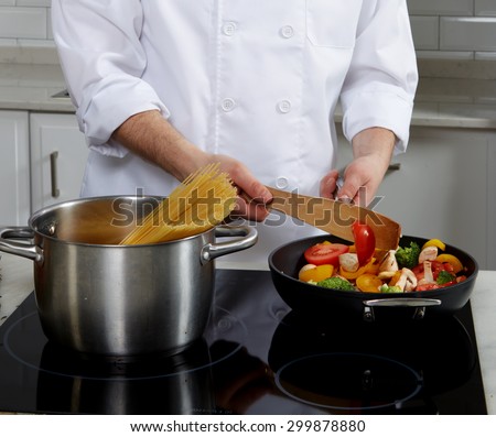 Cook man standing near the plate, cook pasta and puts vegetables and mushrooms in a skillet