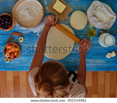 The girl blonde in an apron rolls puff pastry for flan. Cook makes Cake bakery dough and fruit with the addition of cream downed