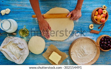 Top view of the girl rolls the dough on a blue vintage table, there are a number plate of mincemeat