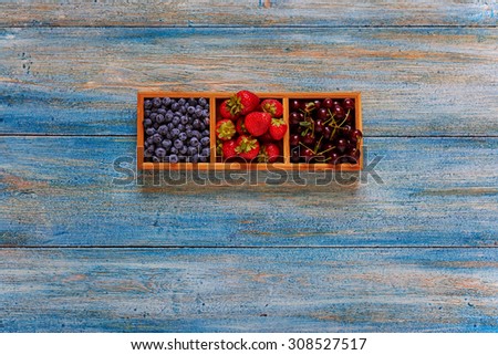 On the vintage wooden desk, cook in style serve berries in a wooden form with separate compartments for berries