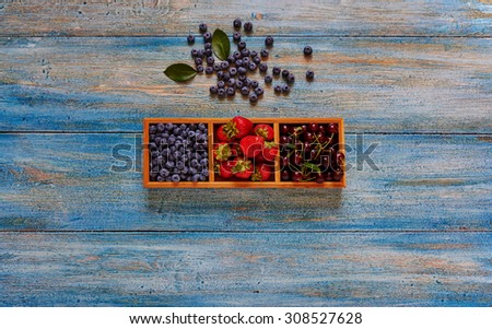Wooden forms with cells which are ripe berries, blueberries in the first cell, the second-filled ripe strawberries and cherries is the third cell