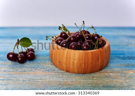 On the wooden kitchen table is a wooden bowl with cherries, which will be used to cook the filling in a cake or bagels