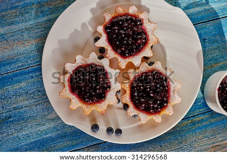 There is tasty dessert is on the kitchen table, vintage, tarts made from unleavened dough with jam neatly on a white circular plate, is seen next to a small bowl with the remaining home-made jam from