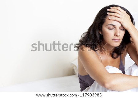 dark haired woman with headache sitting on her bed