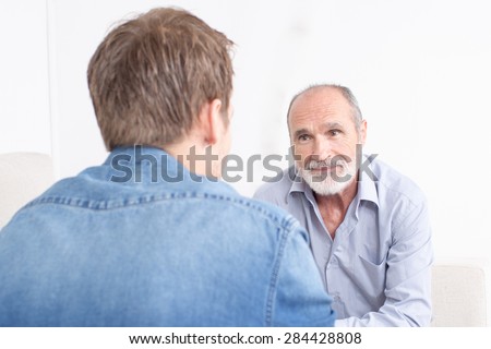 Two man talking while the father is smiling and you can see the son from the back