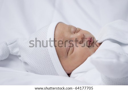 Baby less than one week old. He lays asleep on a white backdrop in white clothing to provide plenty of space for copy. studio set up of one key light and a bounced flash with a shallow depth of field.