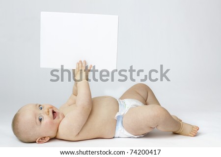 Studio Isolation of an Infant Child. The baby boy is Isolated on white with a Horizontal composition. He is laid on his back smiling into the camera whilst holding a white board in the air.