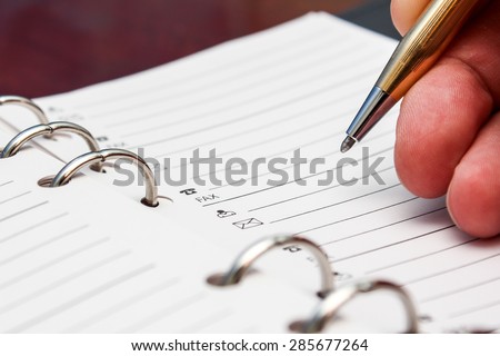 Business man\'s hand with pen writing a contact number or email on the paper of note book