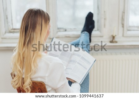 Young blond woman studying with her stockinged feet up on a windowsill above a radiator viewed from behind ストックフォト © 