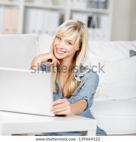 Smiling woman at home with her laptop sitting in her living room browsing the web