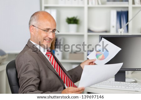 Side view of mature businessman analyzing documents at office desk