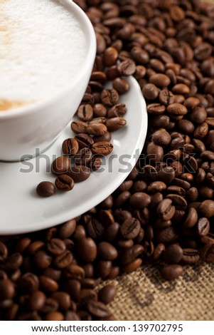 A cup of coffee in saucer with scattered coffee beans