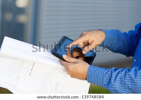 Closeup of architect\'s hands holding blueprint while using digital tablet