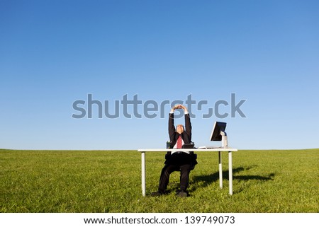 Businessman stretching at desk on grassy field against clear sky